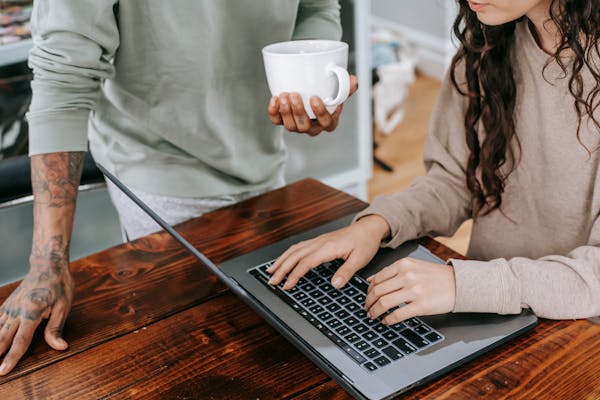 Two people working together at home, one typing on laptop, the other holding coffee.